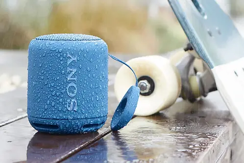 Sony Bluetooth speaker outside with water on the surface next to a skateboard.