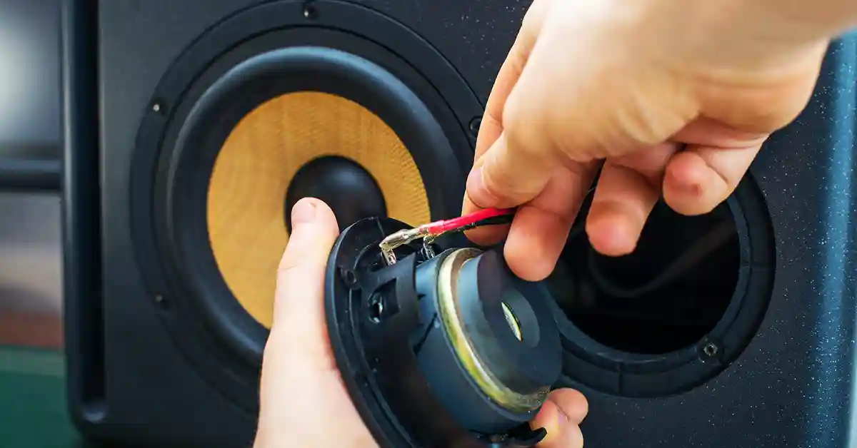 Man fixing a blown speaker from behind by adjusting wires